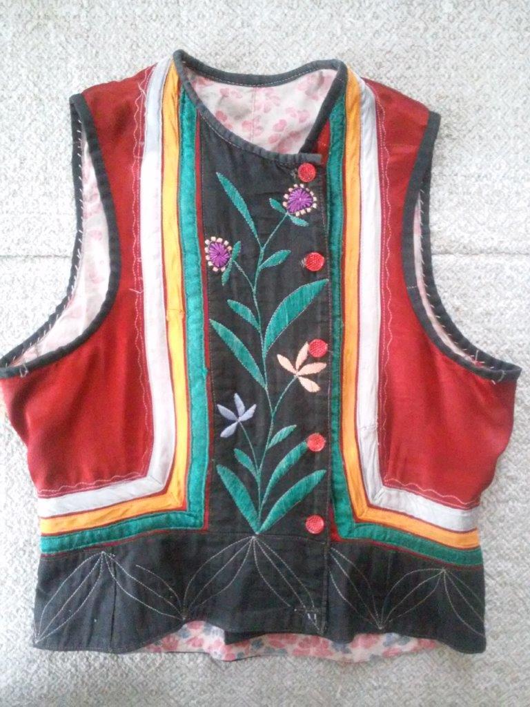 Нагрудник з червоного атласу, оздоблений різнокольоровими стрічками, фігурною машинною вистрочкою та ручною вишивкою гладдю. Рівненська обл., Сарненський р-н, с. Кричильськ. Поч. ХХ ст.